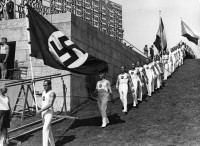 L’entrée des gymnastes allemands aux Jeux de Berlin. Le régime nazi se sert des Jeux de Berlin 1936 pour déployer le drapeau à croix gammée qui remplace la bannière allemande à trois couleurs. 